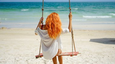 Plaj tatili tropik tarzı palmiye portresi plajda güzel bir kızın mavi salıncakta sallanışı. Kızıl saçlı kadın Phu Quoc adasında sallanıyor, Vietnam. Tropik palmiye ağacında salıncakta mutlu.