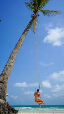 Plaj tatili tropik tarzı palmiye portresi. Plajda sallanan yakışıklı bir adam mavi deniz. Phu Quoc adasında sallanan bir adam, Vietnam. Mutlu adam tropikal palmiye ağacında sallanıyor.