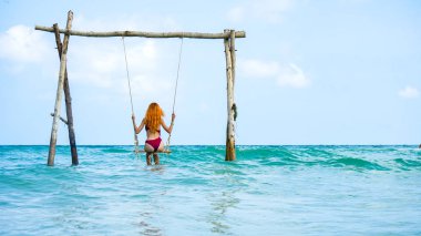 Plaj yaz tatili salıncakta sallanıyor sahilde güzel bir kız mavi salıncakta sallanıyor kızıl saçlı bir kadın sallanıyor Phu Quoc adasında, Vietnam. Tropikal okyanus salıncağında mutlu.