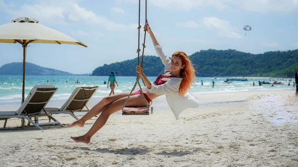 Beach summer vacation tropic palm style portrait of young beautiful girl on beach swing blue sea.Red haired woman swinging on the beach on Phu Quoc island, Vietnam. Happy  on tropical palm tree swing.