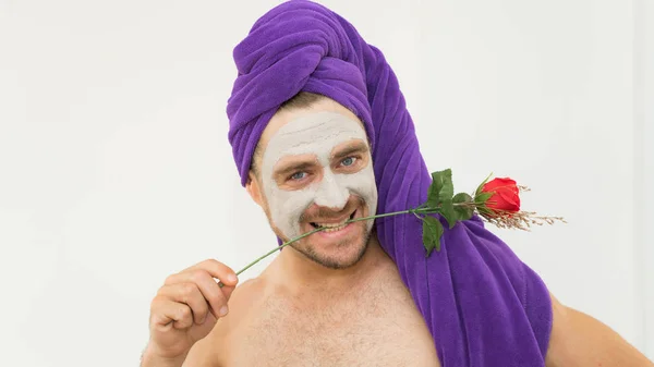 Emotional handsome funny man holding rose in his teeth wearing bath cap and cosmetic mask in his face. Funny crazy man wih rose  for Women day concept .Man copies woman behaviour in comical way.
