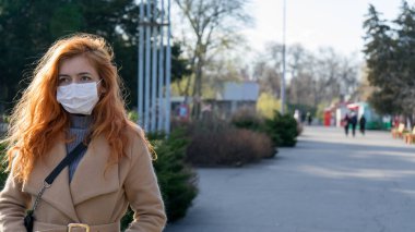 Güzel kızıl saçlı, ameliyat maskesi takan bir kız şehirde salgın yüzünden boş sokaklarda yürüyor. Kadınlar kentteki salgının yol açtığı açık havada yürürken kendilerini korurlar. Virüs koruması..
