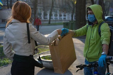 Karantina sırasında teslimatçı kadın alıcıya internetten sipariş vermiş. Genç ve güzel bir kadın siparişini tıbbi maske ve eldivenli neşeli kuryeden alır. Yemek teslimatı konsepti..