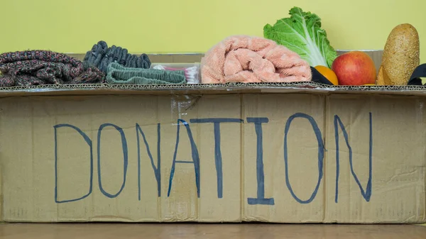 Big donation box with food and clothes insideon yellow background on table. Care for elderly people during the quarantine.