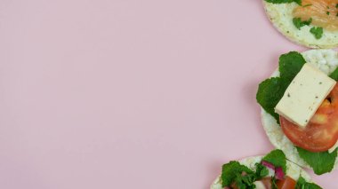 Farklı sağlık malzemelerine sahip üç pirinç keki sağ köşede pembe arka planda oturuyordu. Domatesli pirinç kekleri, somon, nane ve diğer sebzeler orta bölüme yerleştirilmiş..