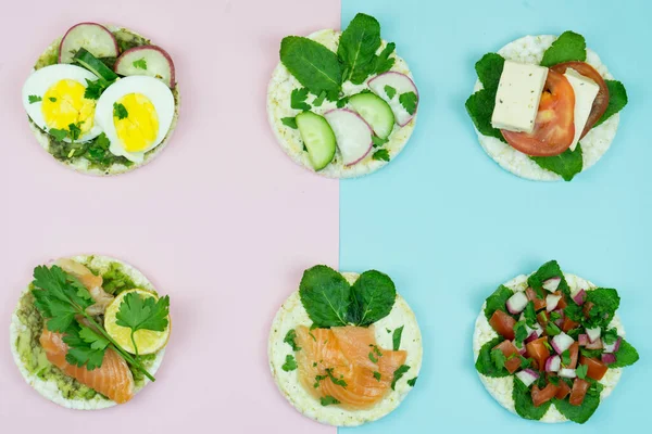 Beautiful six rice cakes sandwiches with different healthcare ingredients on pink and blue background.Tasty rice cakes with tomatoes, salmon, mint and others fit vegetables. Healthcare food concept
