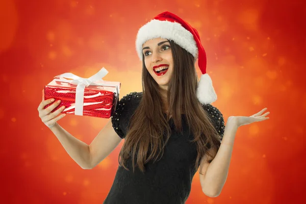 Attraente ragazza sorridente in cappello di Babbo Natale con regalo rosso — Foto Stock