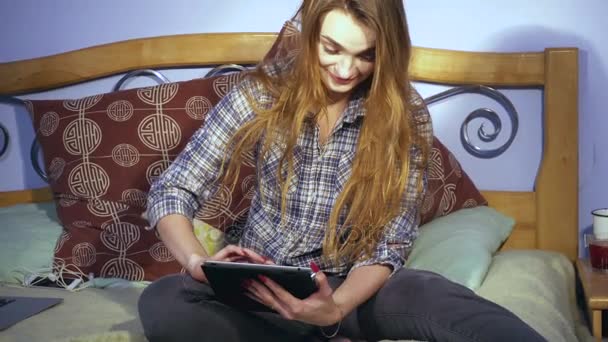 Fille est assis dans le lit regarder dans Tablette et sourit — Video