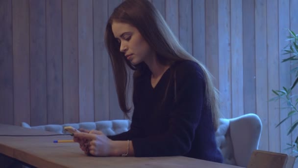 Dziewczyna siedzi przy biurku i patrząc na telefon — Wideo stockowe