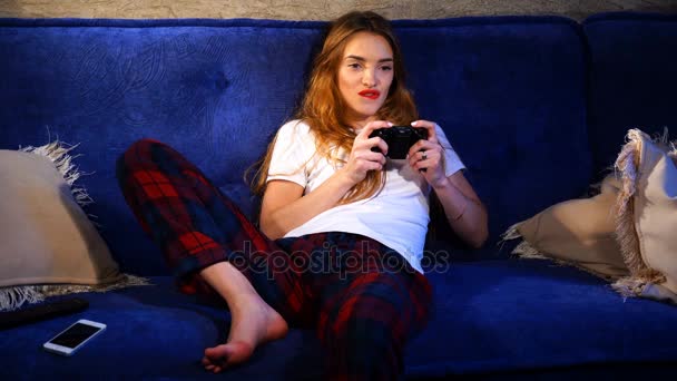 Девушка расслабилась, сидя на диване и играет в компьютерную игру — стоковое видео