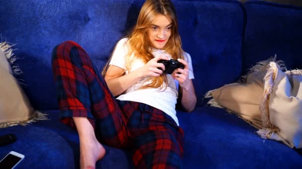 Девушка сидит на диване и играет в компьютерные игры — стоковое видео