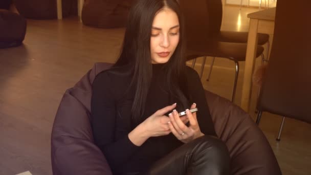 Morena senta-se em uma cadeira e olha para o telefone — Vídeo de Stock