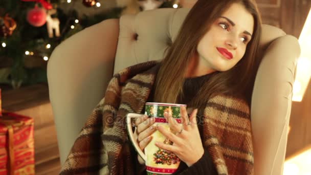 Meisje met deken zit in een stoel en drinken thee uit een kopje kerst — Stockvideo