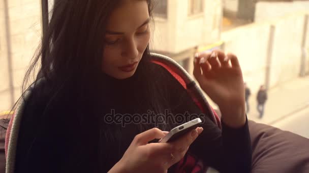 Красивая черноволосая девушка смотрит на телефон и улыбается — стоковое видео