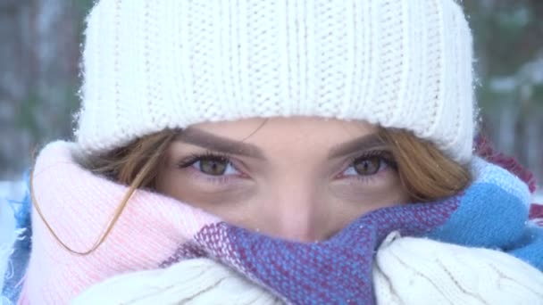 Chica con un sombrero caliente y bufanda mira hacia adelante y parpadea — Vídeos de Stock
