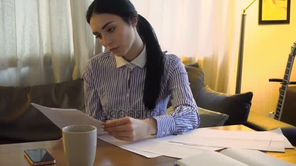 Menina bonita senta-se no escritório e escreve algo no papel — Vídeo de Stock