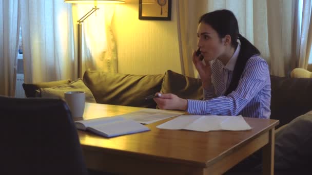 Morena senta-se em seu escritório, segurando uma caneta e falando ao telefone — Vídeo de Stock