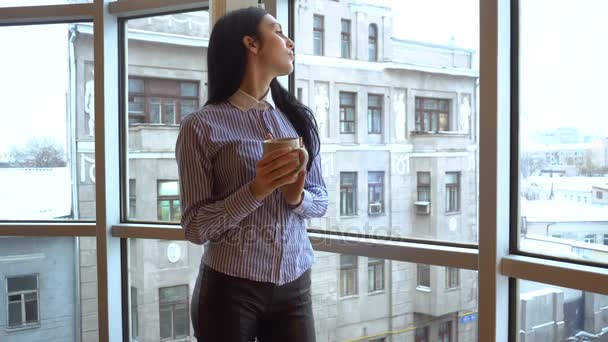 Мила дівчина дивиться у велике вікно і п'є чай — стокове відео
