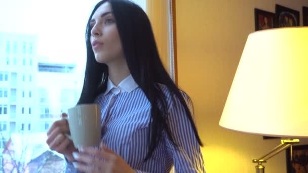 Chica se para, bebe té y mira por la ventana — Vídeos de Stock