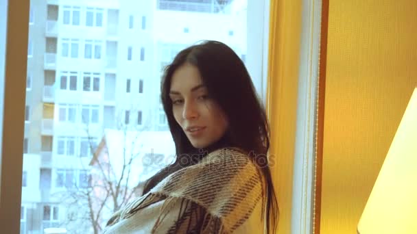 Portrait of a charming young girl with black hair near the window looks away and smiles — Stock Video