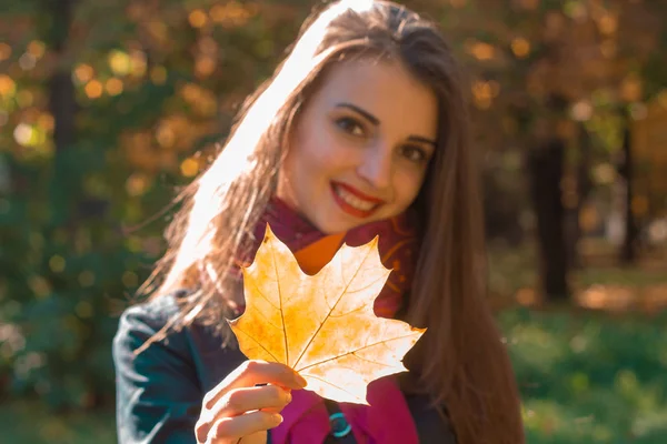 Hermosa chica sonriendo y sosteniendo una hoja de arce en su mano — Foto de Stock