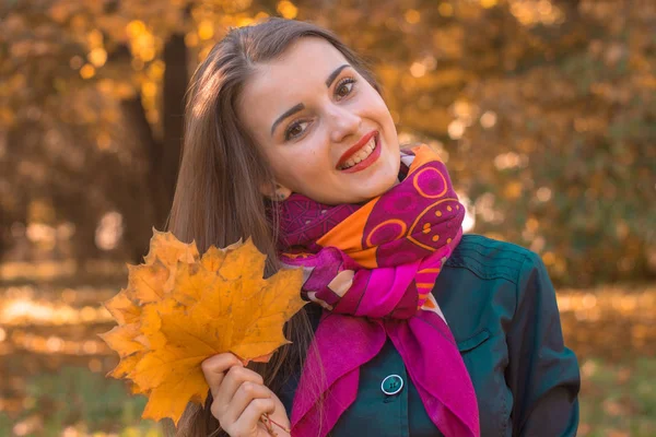 Молодая девушка в Шарфе улыбается и держит кленовый лист в руке — стоковое фото
