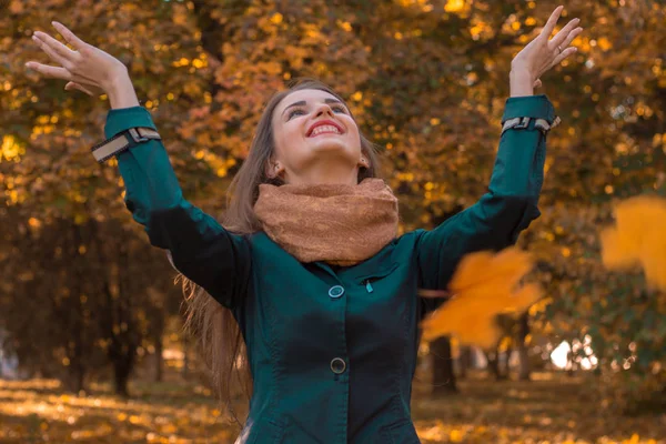 Jong meisje gooit de bladeren in het Park en glimlacht — Stockfoto