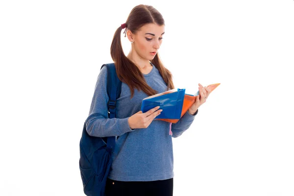 Ung vacker student flicka med ryggsäck läser en bok och poserar isolerad på vit bakgrund i studio — Stockfoto