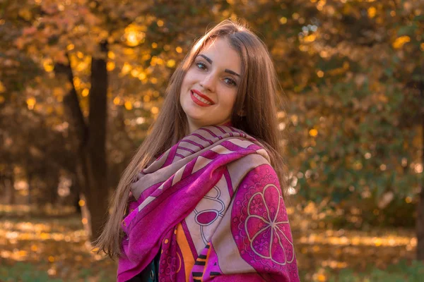 Hermosa joven en una bufanda rosa se encuentra en otoño Parque y sonríe —  Fotos de Stock