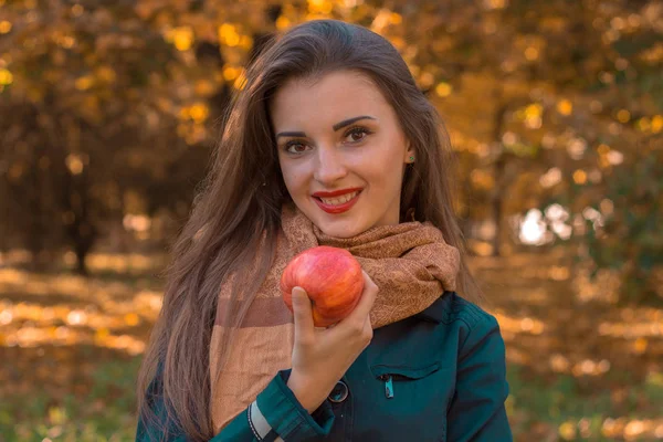Sorridente bella ragazza si trova nel parco e tiene in mano una mela rossa — Foto Stock