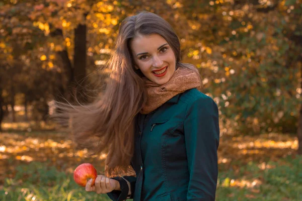 Милая девушка с длинными волосами стоит в парке и держит Apple в руке — стоковое фото