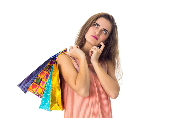 Una joven mira pensativamente a un lado y sostiene bolsas multicolores — Foto de Stock