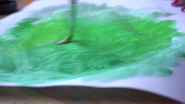 Una chica pinta con un pincel y pintura verde en una hoja de papel — Vídeo de stock