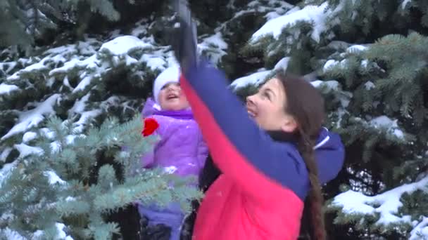 Dívka v její ramena dítěte a setřásá na sněhu s větvemi — Stock video