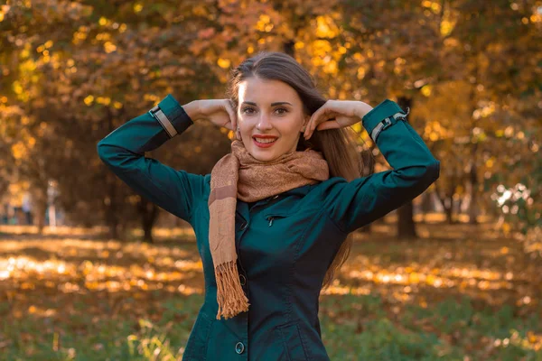 Νεαρό κορίτσι με σκούρο μπουφάν και κασκόλ στέκεται στο φθινόπωρο πάρκο σήκωσε τα χέρια της στο κεφάλι — Φωτογραφία Αρχείου