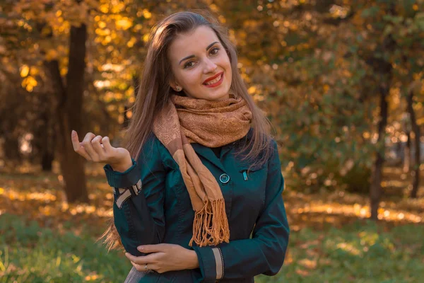 Joven chica alegre con una bufanda en los hombros de los puestos en el parque y sonríe — Foto de Stock