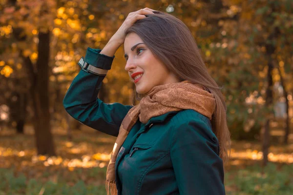 Fille dans une chemise sombre et écharpe se tient sur le côté dans le parc tient les cheveux de la main — Photo