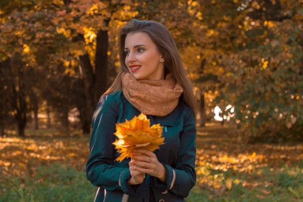Fiatal lány sálat és levelek a kezében néz el a parkban — Stock Fotó
