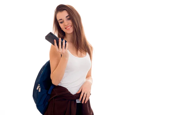 Porträt einer jungen attraktiven Studentin mit blauem Rucksack und Handy in den Händen isoliert auf weißem Hintergrund — Stockfoto