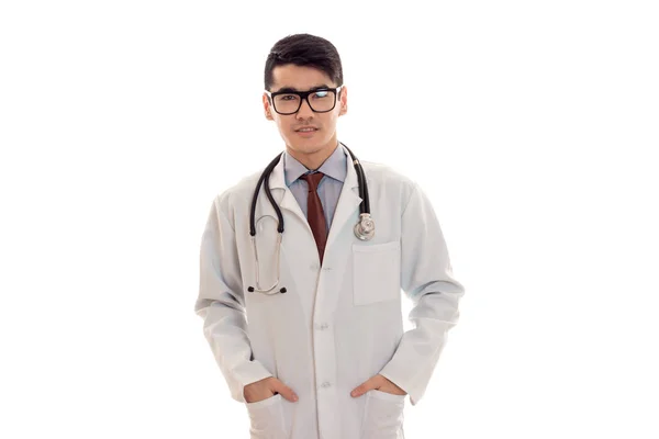 Mladý pohledný muž Doktor pózuje v uniformě a brýle izolovaných na bílém pozadí v studio — Stock fotografie