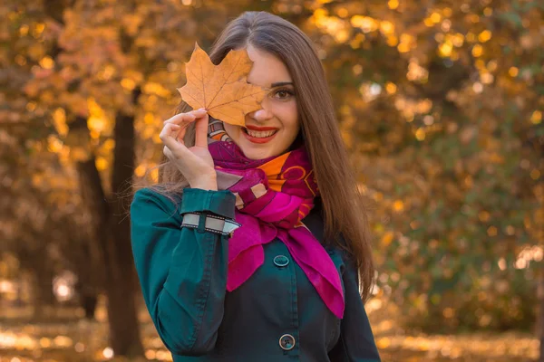 Bonito atraente menina no cachecol rosa mantém a folha perto dos olhos e sorrisos — Fotografia de Stock