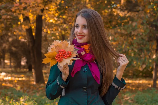 Jovem bonito menina com cabelos longos olha para mantém folhas de Rowan em sua mão e sorri — Fotografia de Stock