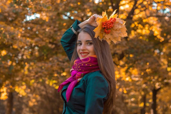 Fiatal aranyos lány rózsaszín fejkendő felemelte a kezét, a levelek fölött a fejét és mosolyog — Stock Fotó