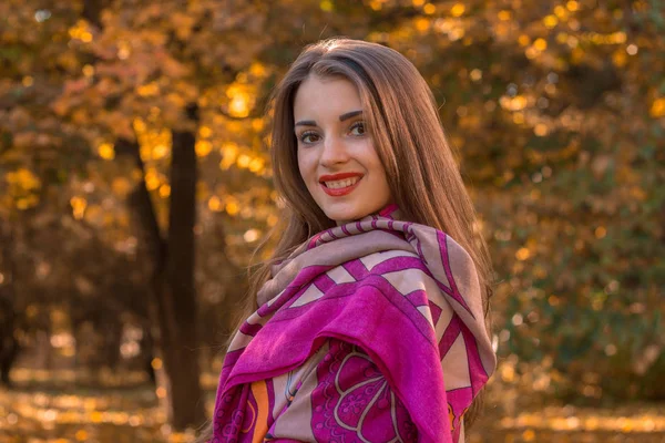 Uroczy młoda dziewczyna z czerwona szminka stoi w parku szalik na ramionach i uśmiecha się do planu krupnyy — Zdjęcie stockowe