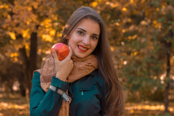 Fiatal gyönyörű lány, hosszú haj, sötét pólót és meleg sál tart alma néz előre mosolyog — Stock Fotó