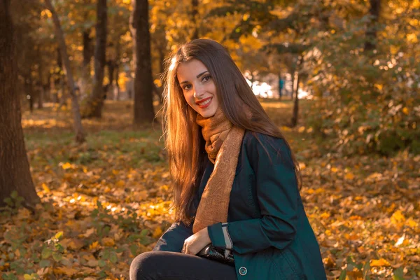 Chica joven con el pelo largo y bufanda sentado en el parque en el césped sonríe — Foto de Stock