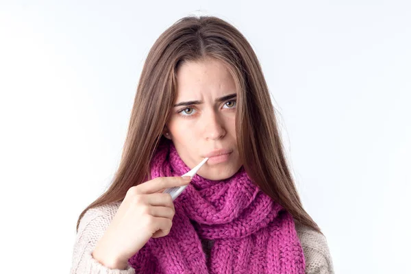 Jeune fille en écharpe chaude regarde droit et garde thermomètre à bouche est isolé sur fond blanc — Photo