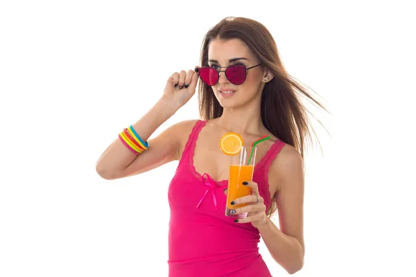 Приваблива молода дівчина в рожевій сорочці та сонцезахисних окулярах п'є апельсиновий коктейль ізольовано на білому тлі — стокове фото