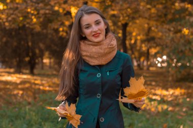 sıcak Fularlı neşeli genç kız sokakta duruyor ve kuru yaprakları elinde tutar