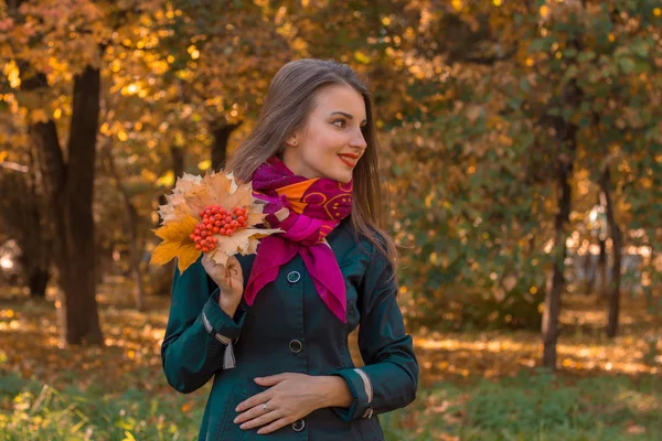 Sorridente ragazza si trova nel parco tiene in mano le foglie e distoglie lo sguardo — Foto Stock